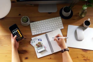 A person reviewing their budget and financial plan with a notebook, calculator, and coffee on a desk, symbolizing the best financial habits to secure their future.