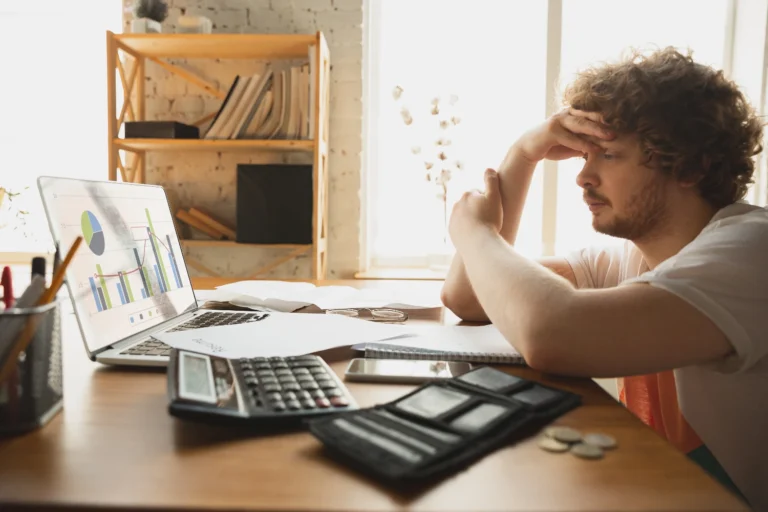 A person overwhelmed by bills, holding a credit card, with scattered coins and receipts on a table, symbolizing poor financial habits.